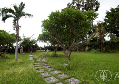 Garden with frangipani trees with path leading towards the beachfront of a villa in Amed, Bali