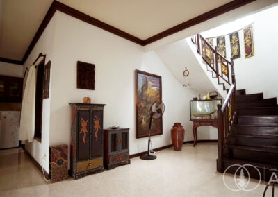 Bottom of teak wooden spiral staircase looking up with Baliniese art on the walls.