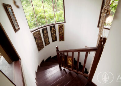 Wooden spiral staircase in with Balinese art on the wall.