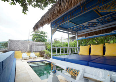 Shaded day-bed with blue cushions next the swimming pool and ocean views