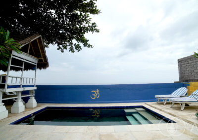 Swimming pool with sun beds and covered day-bed overlooking the beachfront.