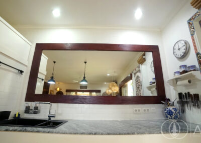 Large wall mirror with wooden frame above the sink in a kitchen with grey marble worktops.