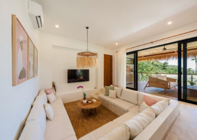 Living room with comfortable sunken sofa and wall-mounted TV. Sliding door open to an outdoor balcony and pictures and hanging on the wall.